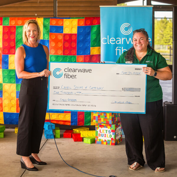 Girl Scouts of Gateway receive $1,000 donation from Clearwave Fiber at a community event. Two people hold a $1,000 check from Clearwave Fiber to Girl Scouts of Gateway, standing in front of colorful LEGO-like blocks.